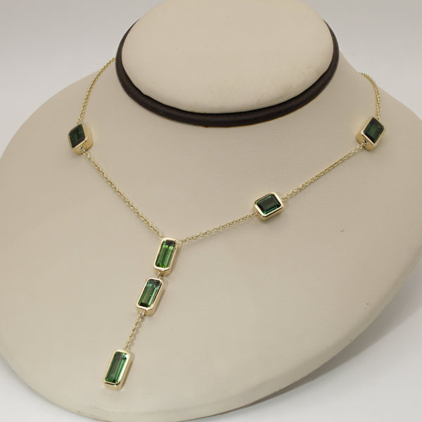 Gold necklace with tourmaline gemstones on a beige neck stand on a white background